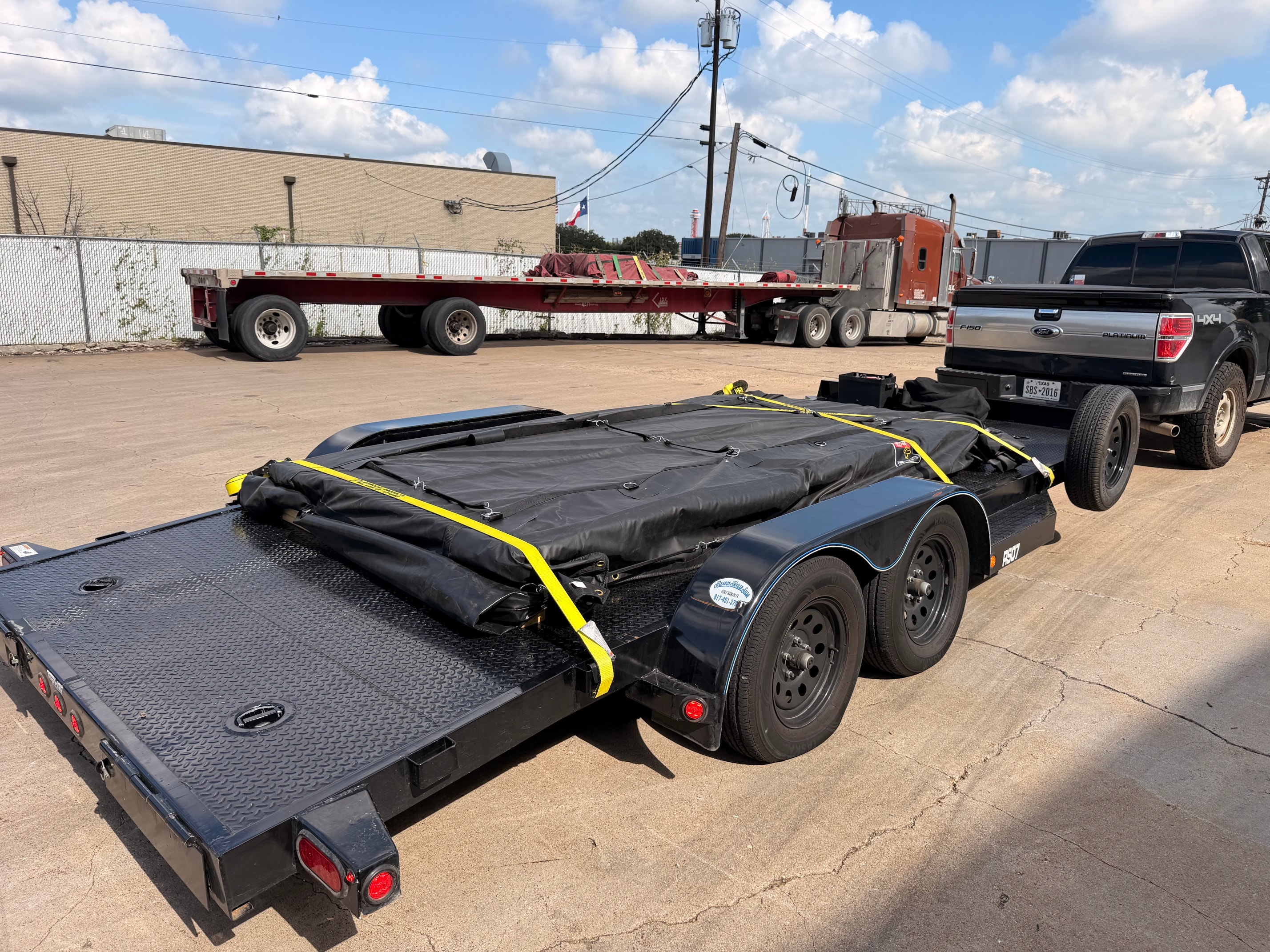 Black flatbed trailer with yellow straps at industrial yard
