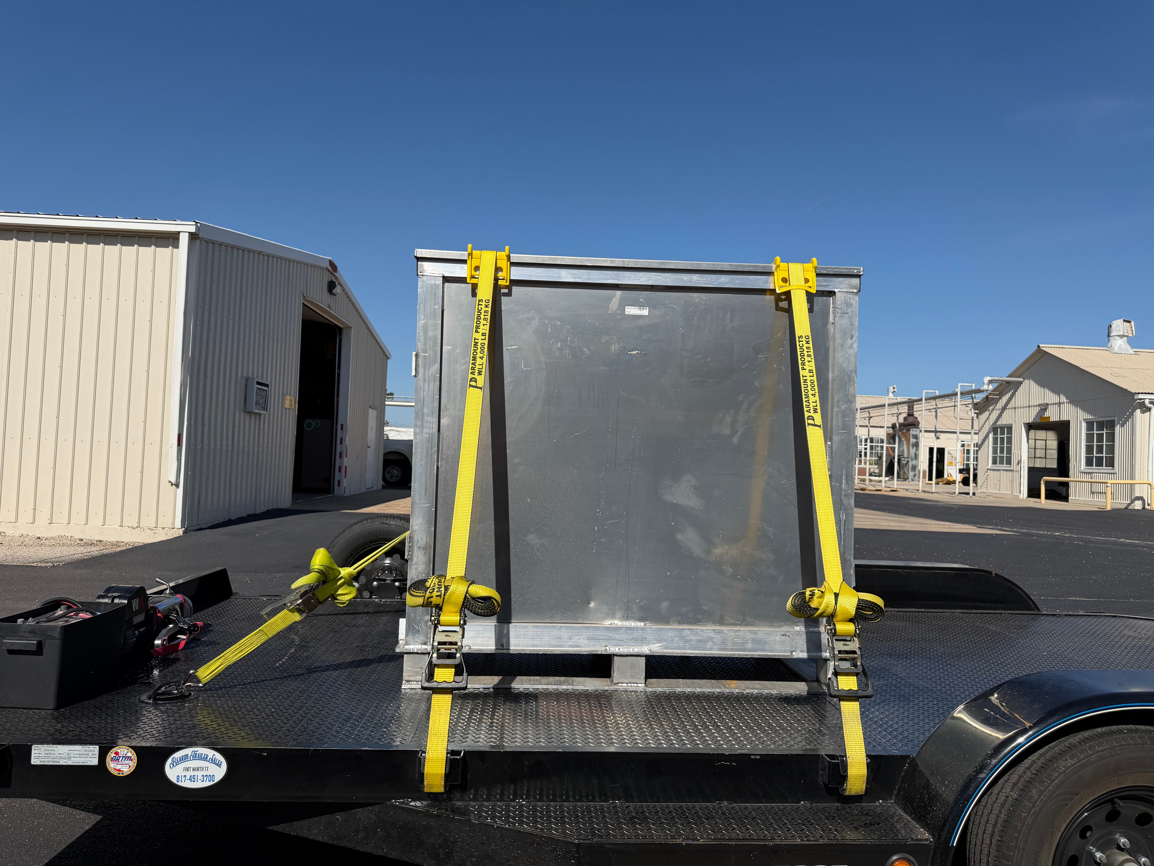 Metal box secured with yellow ratchet straps on flatbed